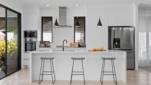 a kitchen with a large white island with bar stools at Pura Villa - Tropical Luxury Living in Palm Cove