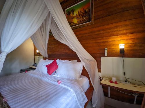 a bedroom with a canopy bed with white sheets and red pillows at Dangin Kubu in Toyapakeh