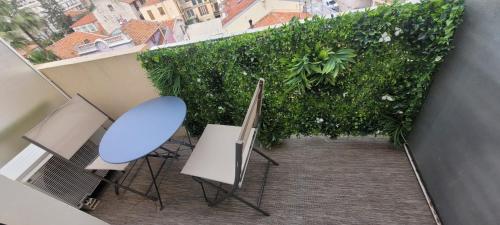 un balcon avec une table et des chaises bleues et une haie verte dans l'établissement rue des roses, à Nice