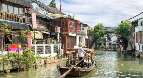 a person in a boat on a river with buildings at Royal Tulip Hotel Zhujiajiao Shanghai in Shanghai