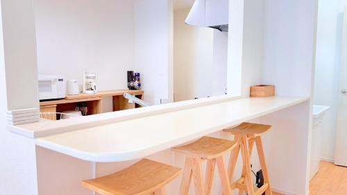a white kitchen with a counter and two wooden stools at Villa Seika -盛夏- in Nago