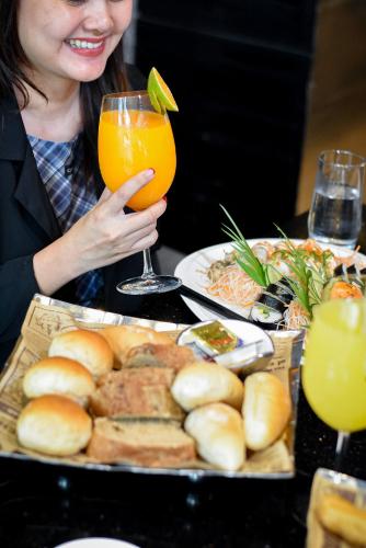 a woman holding a glass of orange juice next to a tray of food at Holiday Inn Bangkok Sukhumvit by IHG in Bangkok
