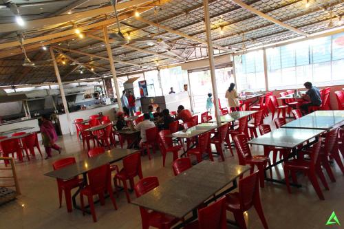 Sai Atithi Resort في شيردي: مطعم بالطاولات والكراسي الحمراء والناس في المطبخ