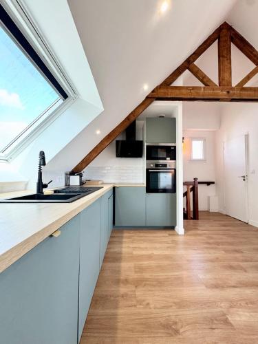 une cuisine avec des placards bleus et une grande fenêtre dans l'établissement Duplex T3 - Au coeur des chênes, à Ploemeur