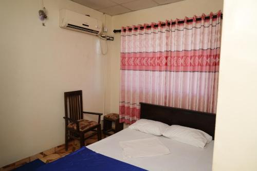 a bedroom with a bed and a window and a chair at Hotel Sella in Kilinochchi