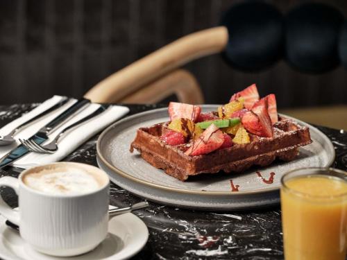 a plate of waffles with fruit and a cup of coffee at Mövenpick Grand Hotel Wroclaw in Wrocław
