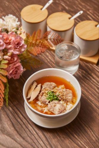 a bowl of soup on a wooden table with flowers at Bansuay Phranangklao Apartment&Hotel in Ban Sai Ma