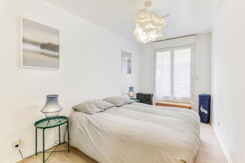 a white bedroom with a bed and a chandelier at Cosy T2 à 100m de la Gare, parking gratuit, WiFi Fibre pour 4 personnes in Saint-Cyr-lʼÉcole