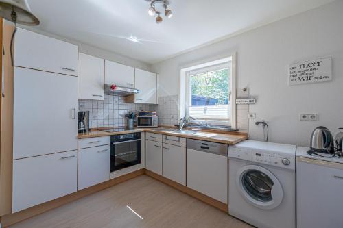 a kitchen with white cabinets and a washer and dryer at Ferienhaus Nordlicht in Steinbergkirche