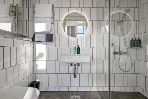 a white tiled bathroom with a sink and a mirror at Unity Helsinki - A Studio Hotel in Helsinki