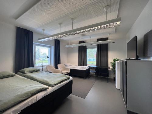 a bedroom with two beds and a desk and a tv at Kotimaailma - Vihtyisä Hostelli in Kokkola