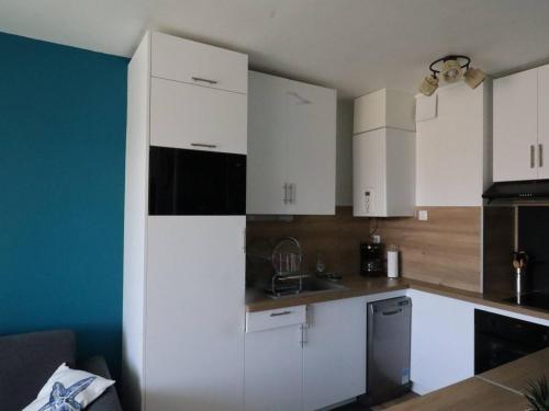 une cuisine avec des armoires blanches et un mur bleu dans l'établissement Appartement charmant à Royan - 4 pers, proche marché, balcon, ascenseur, équipements bébé - FR-1-738-13, à Royan
