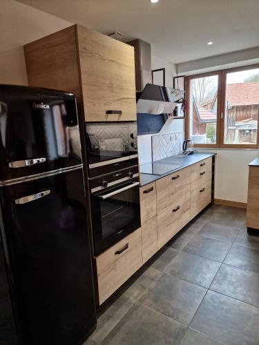 une cuisine avec un réfrigérateur noir et des armoires en bois dans l'établissement Duplex la Beun, à Saint-Paul-en-Chablais