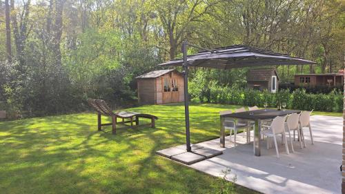 a table and chairs under an umbrella in a yard at Luxe wellnesshuis Drenthe met sauna, whirlpool en omheinde tuin VP048 in Hoogersmilde
