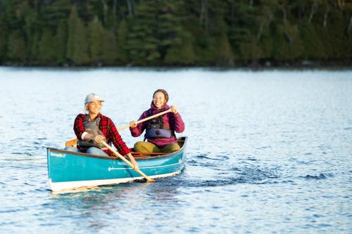 two people are rowing a boat on a lake at voco Saranac Lake NY - Waterfront by IHG in Saranac Lake