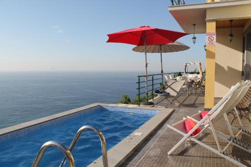 a swimming pool with chairs and a red umbrella at OurMadeira - Casa Jardim Mar, seaviews in Ponta do Sol
