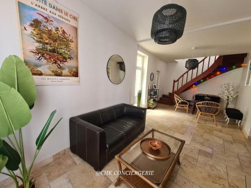 a living room with a black leather couch and a table at Dors Fée Duplex avec Toit-Terrasse et Salle de Jeux - Centre Bourg à 4 min du Puy duFou in Les Épesses