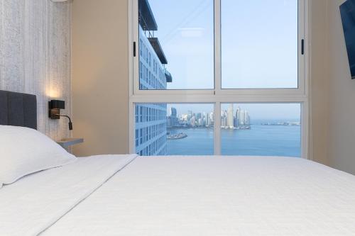 a bedroom with a white bed and a large window at The Sands Apartments By Acomodo in Panama City