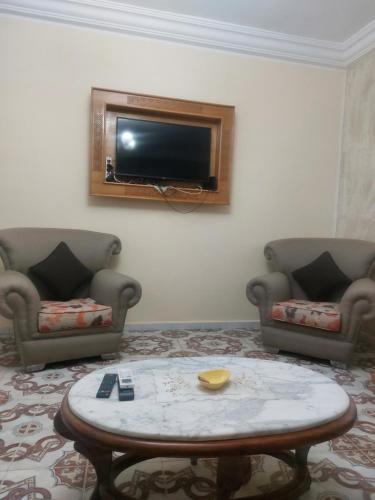 ein Wohnzimmer mit zwei Stühlen und einem Tisch und einem Fernseher in der Unterkunft Zoubeir's 3BR famille home-near shops&transport in tunis cité ettahrir in Bin Rhilouf