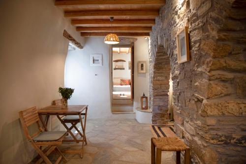 a room with a table and chairs and a stone wall at Under The Linden Tree Tinos in Xinára