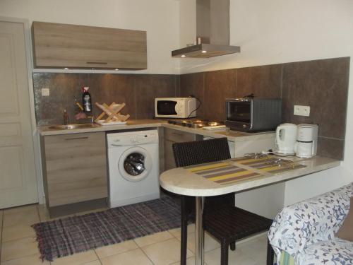 une cuisine avec une machine à laver et une table avec des chaises dans l'établissement Petit appartement plein pied 2 pers AVEC TERRAIN proche Aurillac, à Ytrac