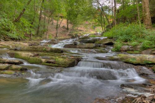 a creek with rocks and waterfalls in a forest at Waterfalls Edge by Venture Smoky Mountains in Pigeon Forge