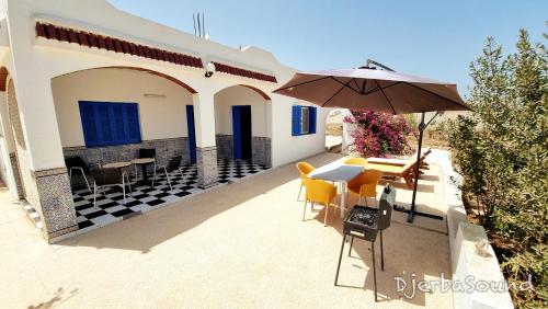 a patio with an umbrella and a table and chairs at Villa milka DjerbaSound in Taguermess
