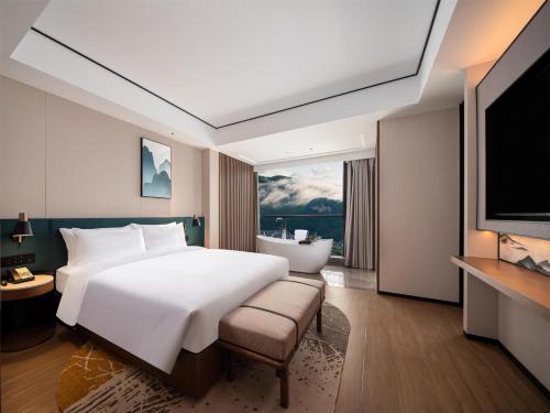 a bedroom with a large white bed and a bath tub at Hilton Garden Inn Zhangjiajie Wulingyuan in Zhangjiajie