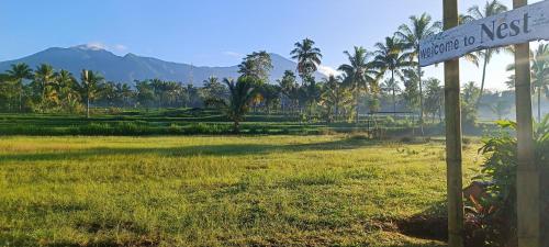 a street sign in a field with palm trees and mountains at Nêst Guesthouse Tetebatu in Tetebatu