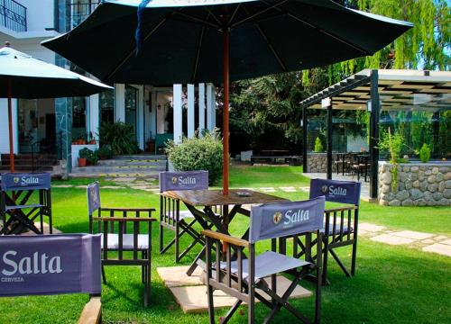 a table and chairs with an umbrella in the grass at Hotel Los Sauces in Cafayate