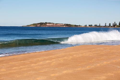 a wave in the ocean next to a sandy beach at Nightelier Narrabeen in Narrabeen