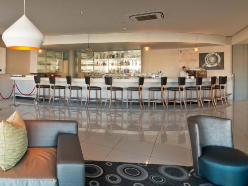 a lobby with a bar with chairs and a man standing at a counter at Krystal Beach Hotel in Gordonʼs Bay