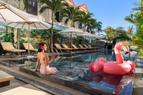 a woman in a pool with a pink swan in the water at ELC Boutique Hoi An Hotel in Hoi An
