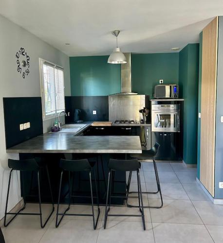 une cuisine avec des murs verts et un îlot de cuisine avec des tabourets dans l'établissement Villa proche mer, montagne, Espagne, à Sallèles-dʼAude