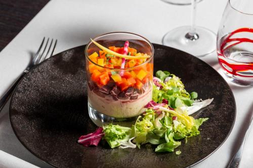 a black plate with a salad and a cup of food at Château Hôtel Du Colombier in Saint Malo