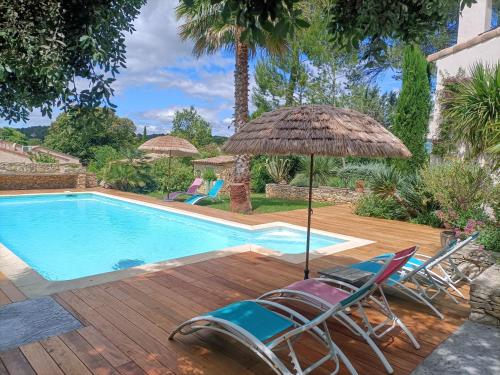Un grupo de sillas y una sombrilla junto a una piscina. en Sous les pins, en Nages-et-Solorgues