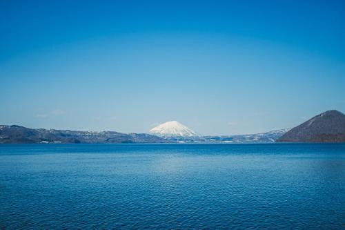 a large body of water with a mountain in the background at 北海道伊達の海辺ヴィラ 最大7名一棟貸切 ファミリー向け 北斎アート in Date