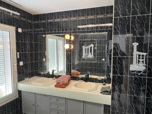 - une salle de bains carrelée de noir avec deux lavabos et un miroir dans l'établissement Le Clos de MANVAL, à Saint-Cyr-sur-le-Rhône