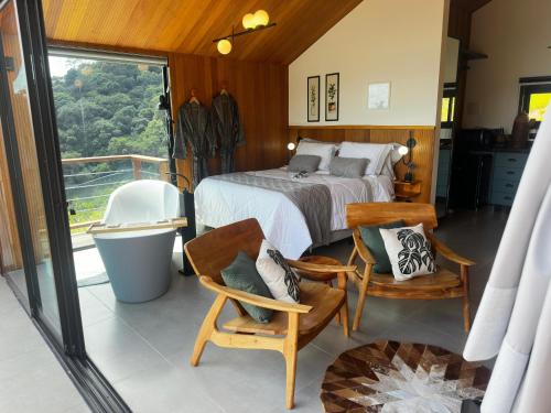 a bedroom with a bed and chairs and a balcony at Cabana Nórdica com Maravilhosa Vista da Serra in Gonçalves