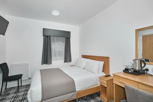 a bedroom with a bed and a desk with a television at Best Western Greater London in Ilford