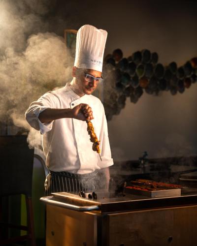 a man in a chefs hat cooking food on a grill at Novotel Kolkata Hotel and Residences in Kolkata