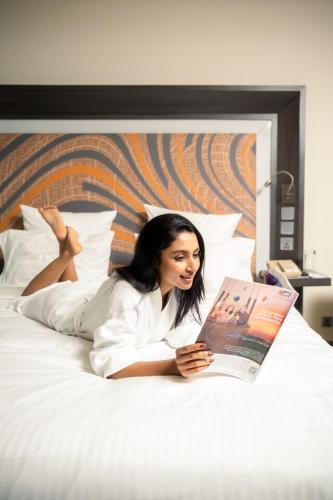 a woman laying on a bed reading a magazine at Novotel Kolkata Hotel and Residences in Kolkata