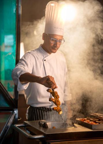 a man in a chefs hat preparing food on a grill at Novotel Kolkata Hotel and Residences in Kolkata