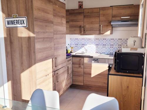 Il comprend une cuisine avec des placards en bois et une télévision. dans l'établissement Appartement lumineux 2 chambres à Wimereux, proche plage, avec garage et Wi-Fi - FR-1-675-13, à Wimereux