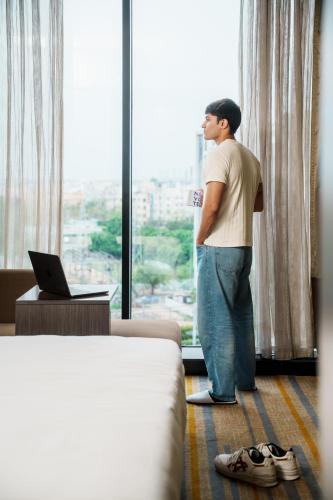 a man looking out the window of a hotel room at Novotel Kolkata Hotel and Residences in Kolkata