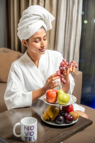 a woman sitting at a table with a plate of fruit at Novotel Kolkata Hotel and Residences in Kolkata