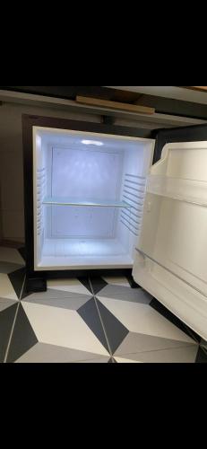 un réfrigérateur vide avec sa porte ouverte sur un sol carrelé dans l'établissement CHAMBRE COCOONING centre ville des Sables D'Olonne quartier Gare Saint Michel située à 1 kilomètre du remblai, à Les Sables-dʼOlonne