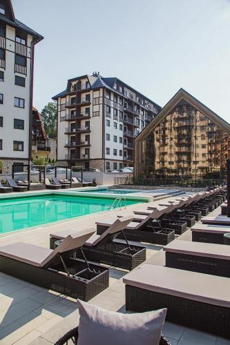 a large swimming pool with lounge chairs and buildings at Apartman Lux Titova Vila Plus Sony PS in Zlatibor