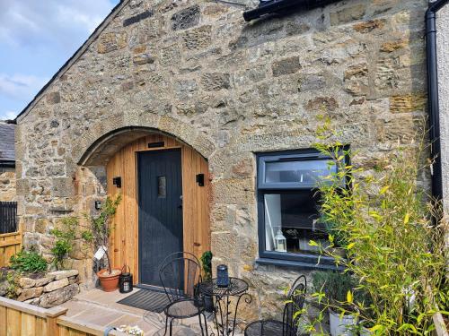a stone house with a black door and a window at Cosy Coach House in Bellingham