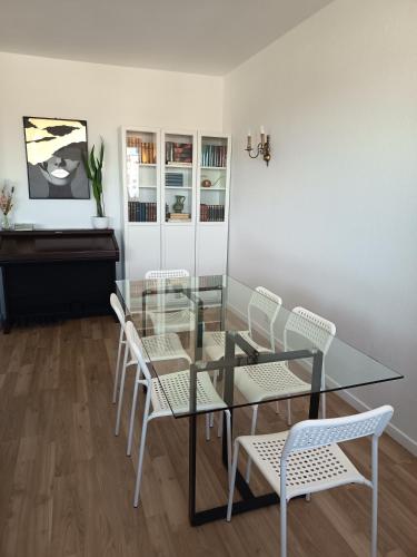une salle à manger avec une table en verre et des chaises blanches dans l'établissement Appartement centre ville Mulhouse, à Mulhouse